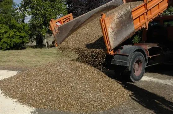 Camion-benne orange déversant des granulats sur une aire extérieure