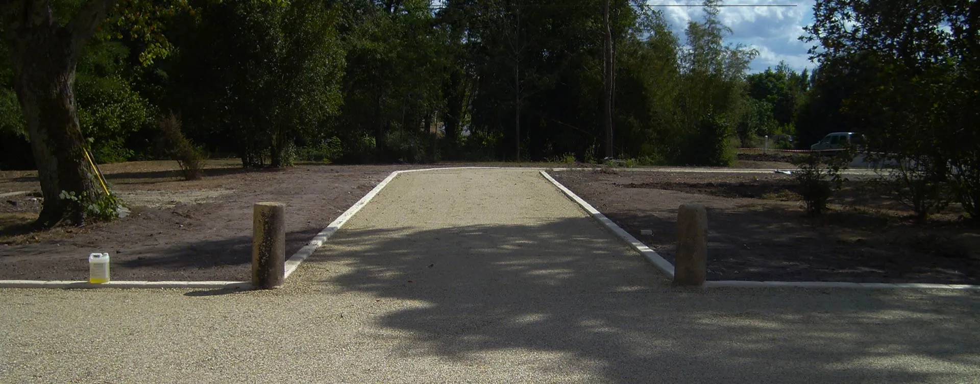Allée en granulats clairs bordée de béton dans un espace arboré.